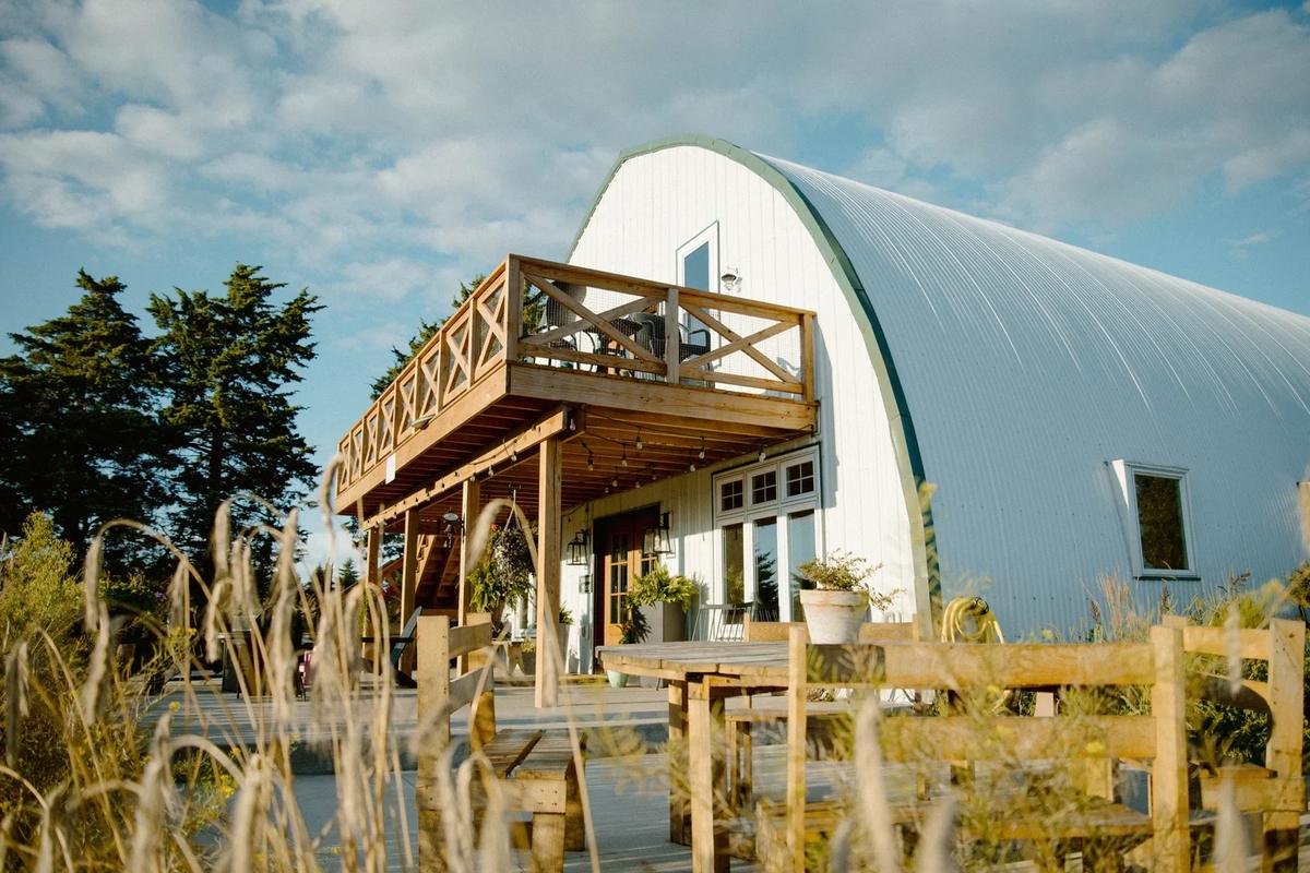 A white barn-style house with a curved metal roof and wooden deck